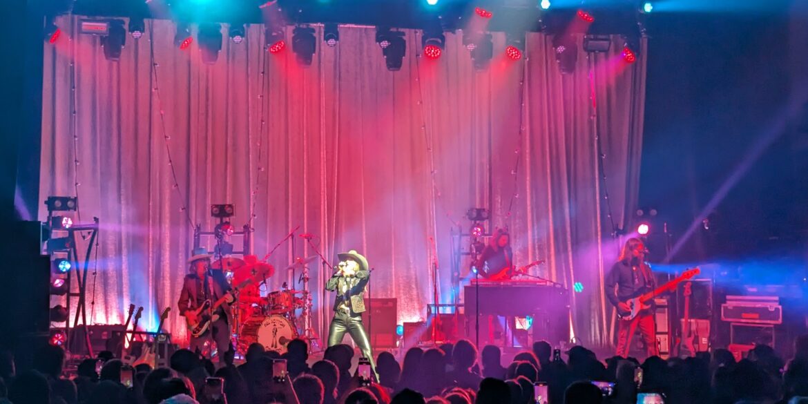 Photo of Lainey Wilson on stage with her band around her.