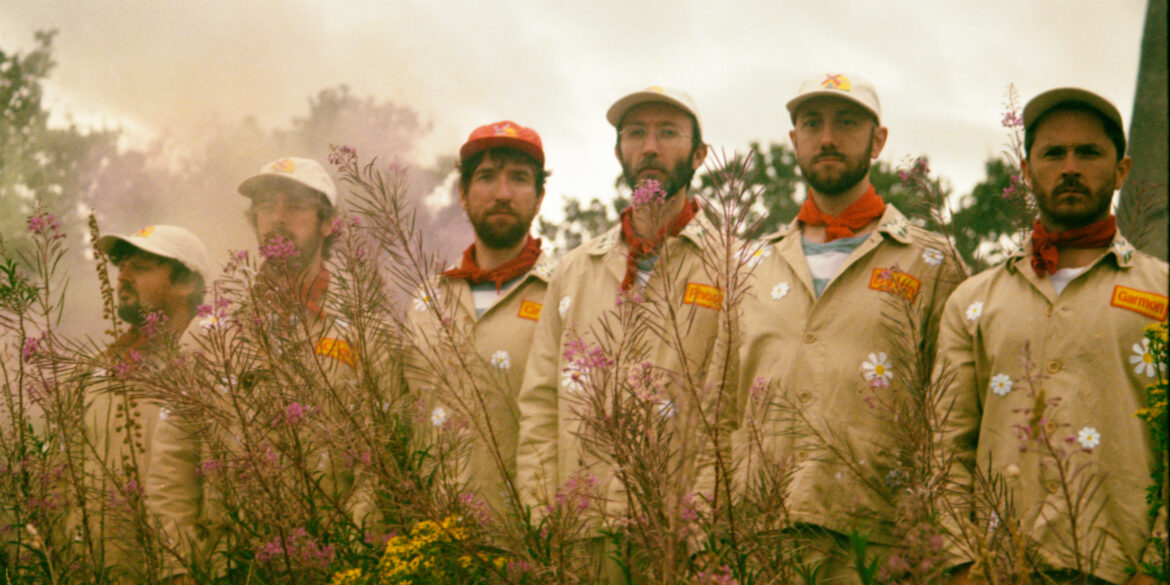 Six men in boiler suits standing in front of a mill.